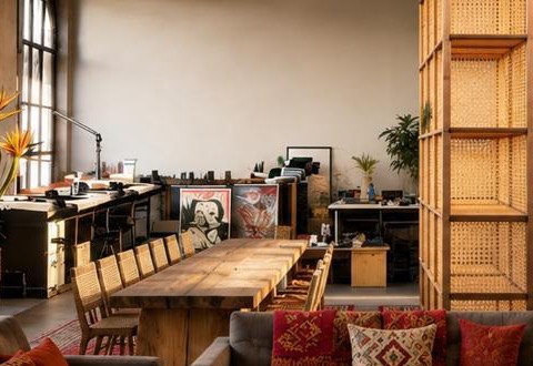 The communal workshop table lined with cane-back chairs, artwork leaning against the wall